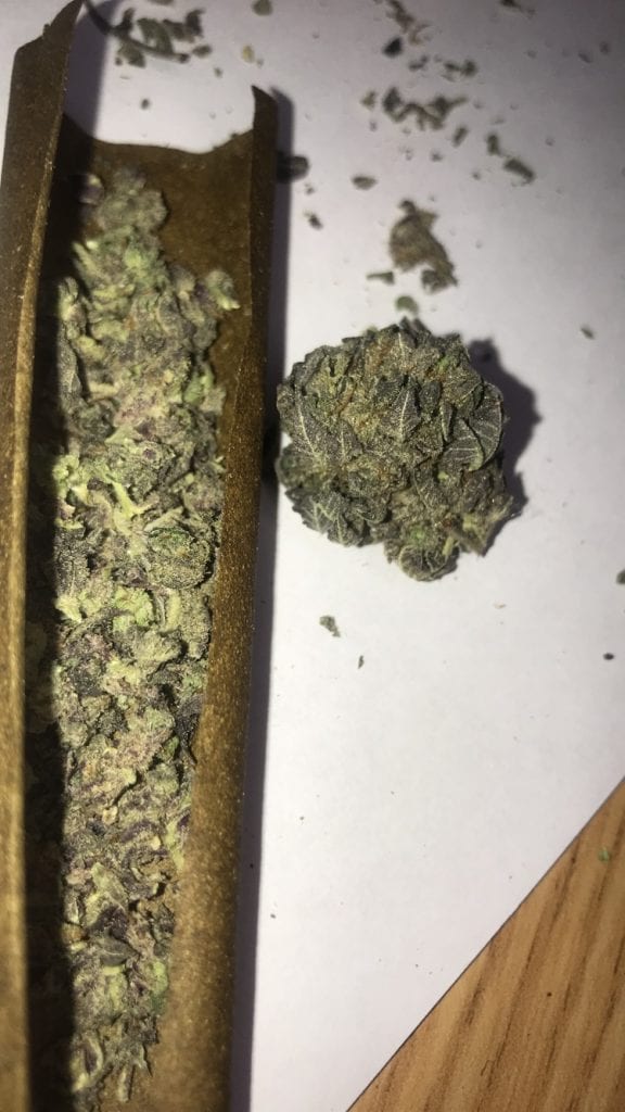 A blunt wrap filled with purple weed on a wooden table. 