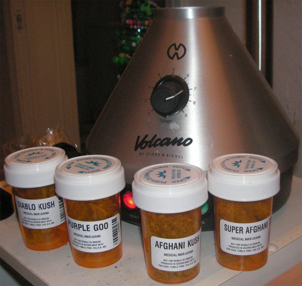 A volcano vaporizer that is a grey metallic colour. Has bottles of cannabis beside it. 