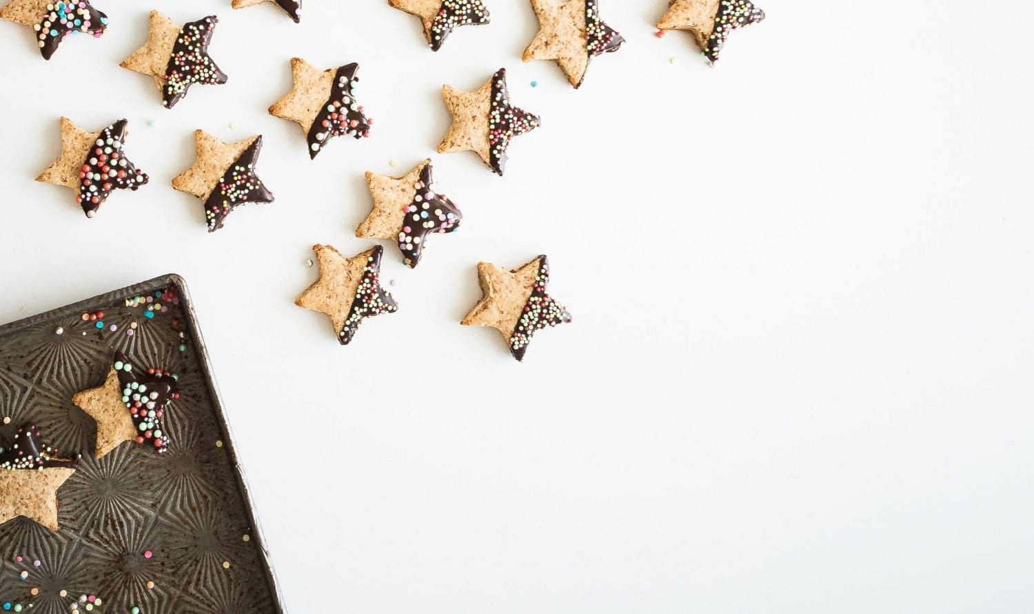 star shaped cookies, half covered in chocolate and sprinkles. alligned artistically with some on baking tray and some on a white table
