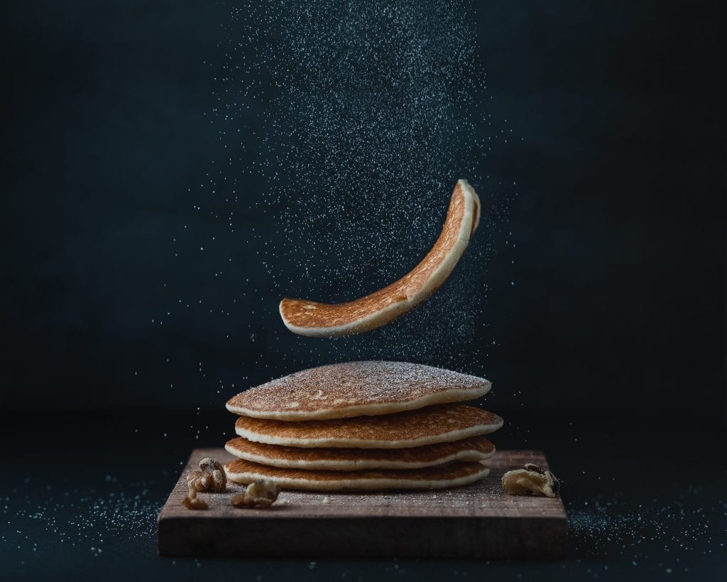 Stack of pancakes with one pancake falling on top of the stack. Black backdrop