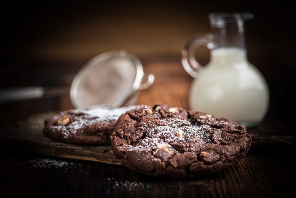 Double chocolate chip cookies sitting in front of a glass of white milk. 
