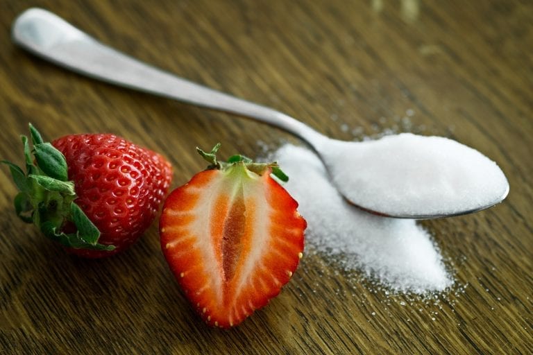Cannabis infused sugar in a spoon on a table with a strawberry beside it.