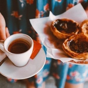 Woman holding a cup of coffee and a plate in one hand and cannabis infused butter tarts on a plate in the other