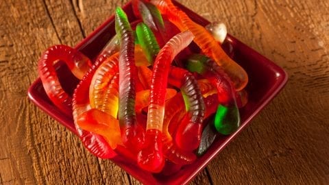 Colourful Fruity cannabis Gummy Worm Candies in a red bowl on a wooden tabe