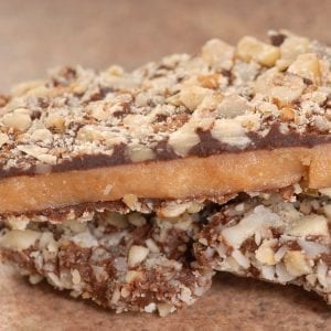 Homemade infused Chocolate English Toffee Topped with Nuts stacked on other pieces of toffee on a brown table