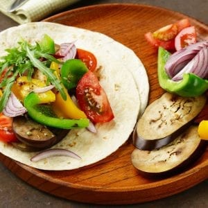 Cannabis infused fajitas With veggies besides them on a wooden plate
