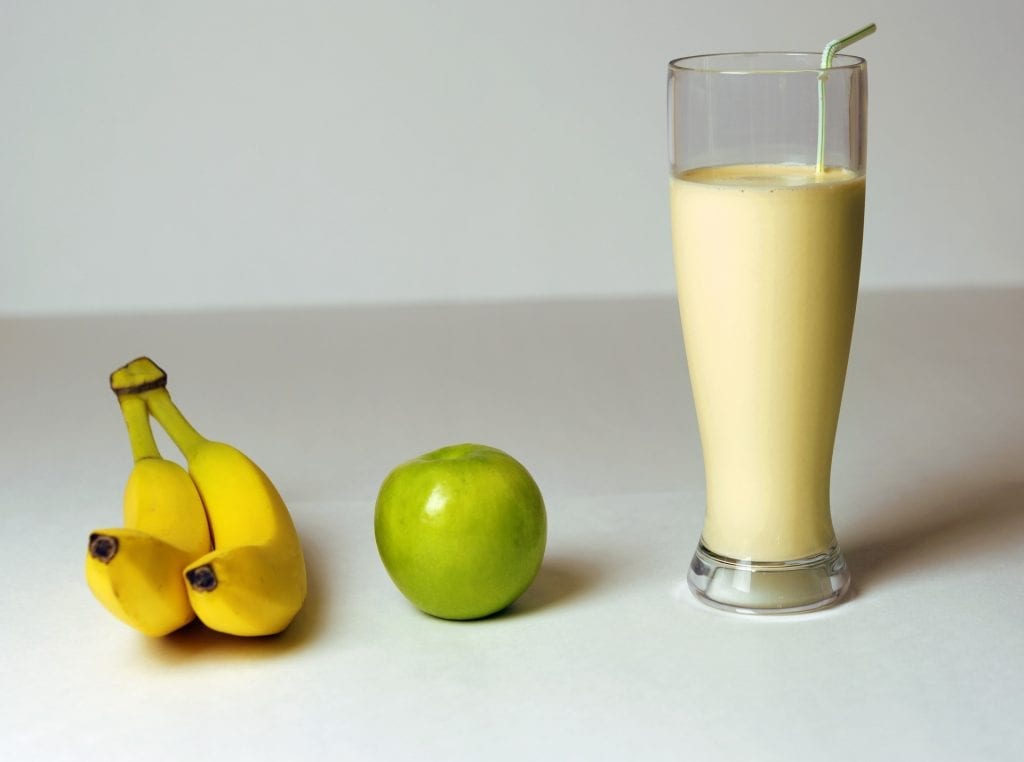 Cannabis infused banana smoothie on the white table with a green apple and two bananas beside it. a weed edible drink recipe.