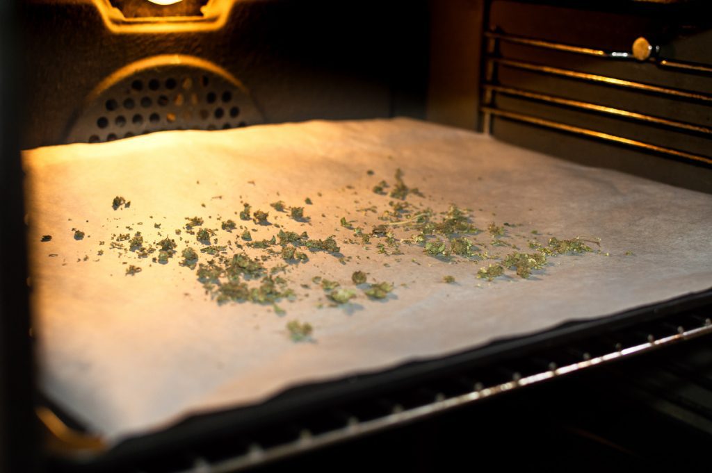 Cannabis trim decarboxylating in a oven on a baking sheet lined with parchment paper. 