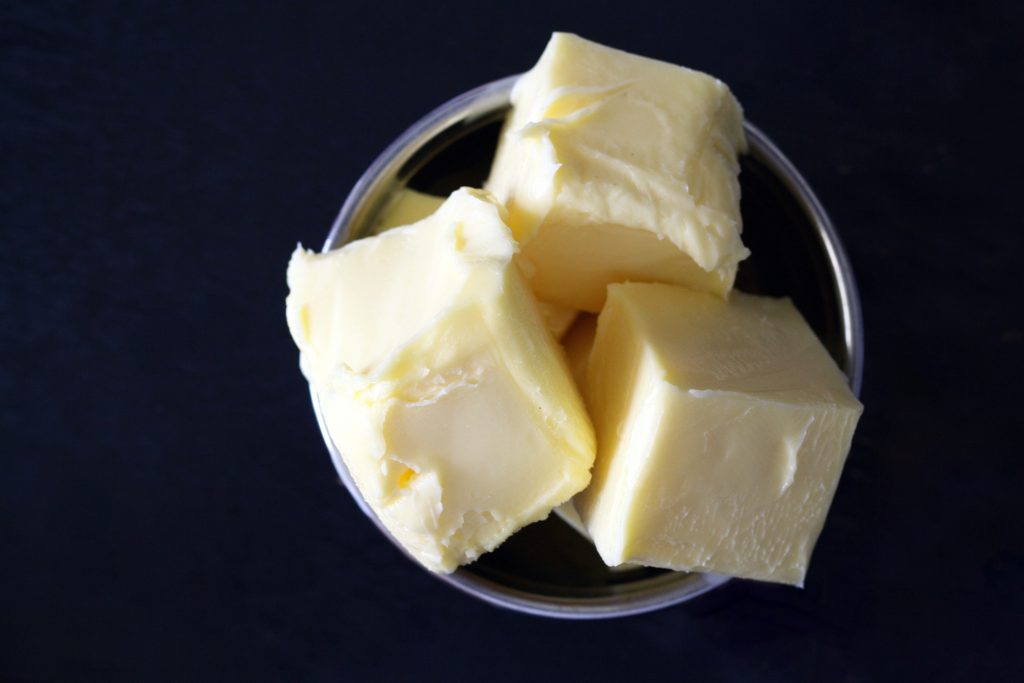 Butter cut into evenly sized square cubes that sit inside a glass bowl. 