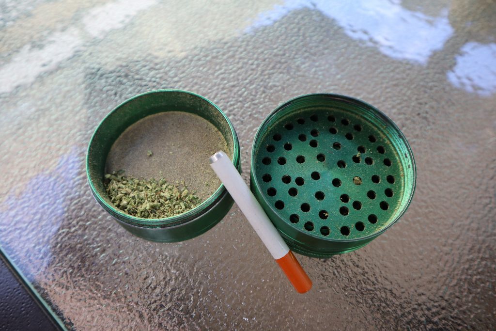 A green weed grinder with a one hitter leaning up beside it. 